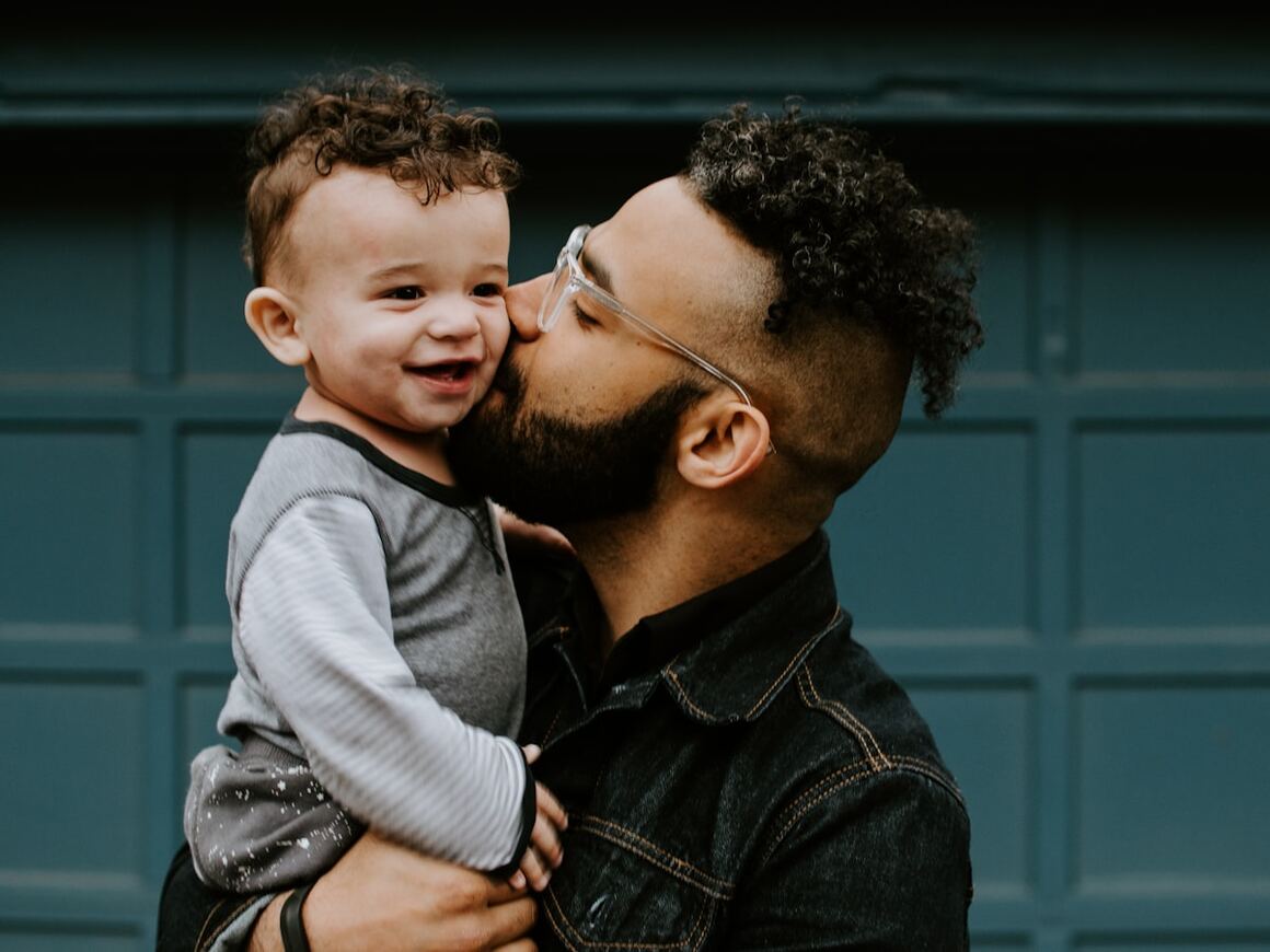 A parent holding their young child close, outdoors in warm light.